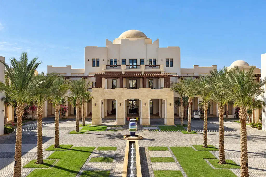 KI-Illustration: Hauptgebäude mit Kuppel und gepflastertem Hof im Ancient Sands Golf Resort & Residences