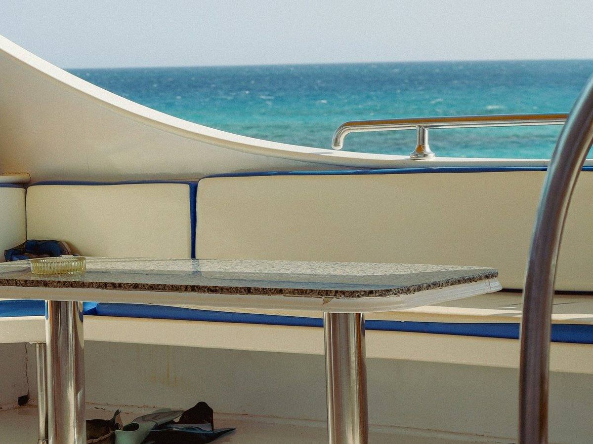 Deck eines Ausflugsboots mit gepolsterter Sitzbank, Tisch und Schnorchelflossen, dahinter das türkisblaue Meer vor Hurghada