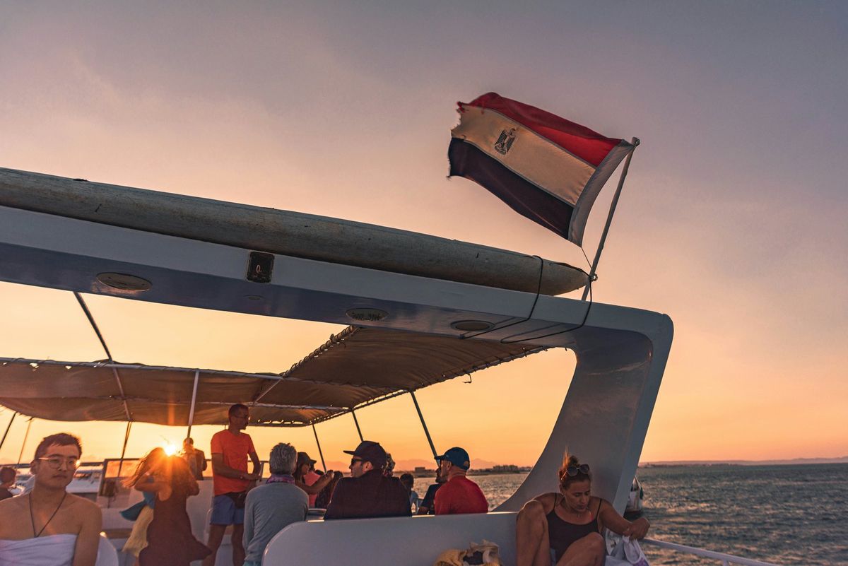 Ausflugsboot mit ägyptischer Flagge und Gästen bei Sonnenuntergang auf dem Meer vor Hurghada
