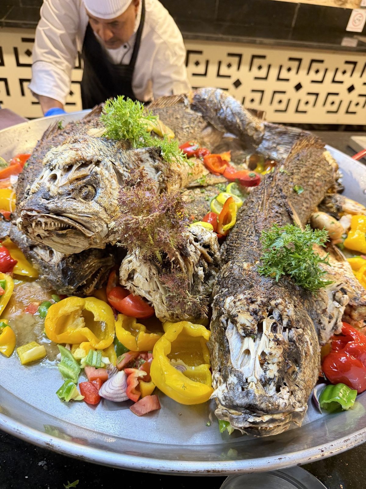 Koch serviert gegrillten Fisch mit Paprika, Tomaten und Kräutern auf einer großen Platte