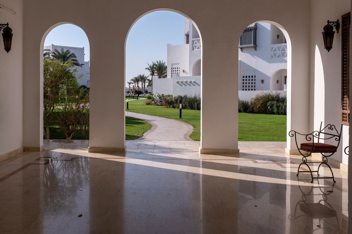 Blick durch weiße Bögen einer Hotellobby auf Garten und weiße Gebäude