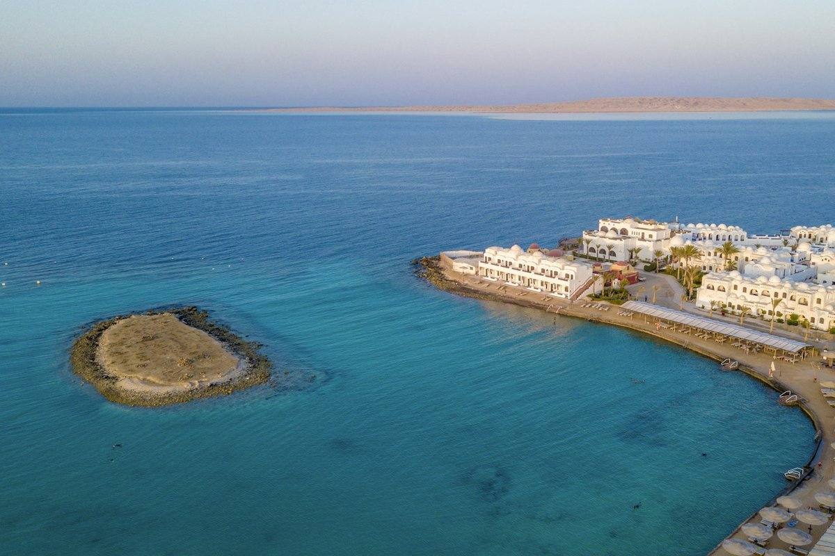 Luftaufnahme einer kleinen Sandinsel vor einer weißen Hotelanlage in Hurghada, am Horizont eine größere flache Insel