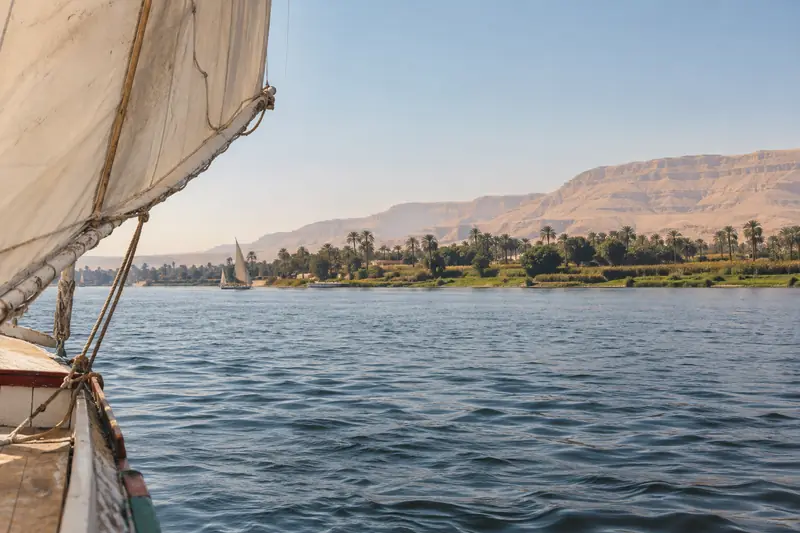 Segelboot auf dem Nil vor Palmen und trockenen Bergen bei Luxor