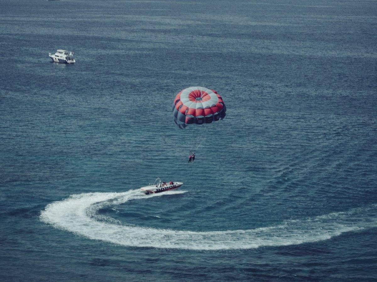 Motorboot zieht beim Parasailing einen rot-weißen Schirm mit zwei Personen über das Meer bei Ain Sokhna