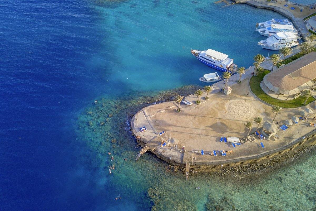 Luftaufnahme einer Landzunge bei Hurghada mit flachem Riffdach, Badestegen, Schnorchlern und Ausflugsbooten