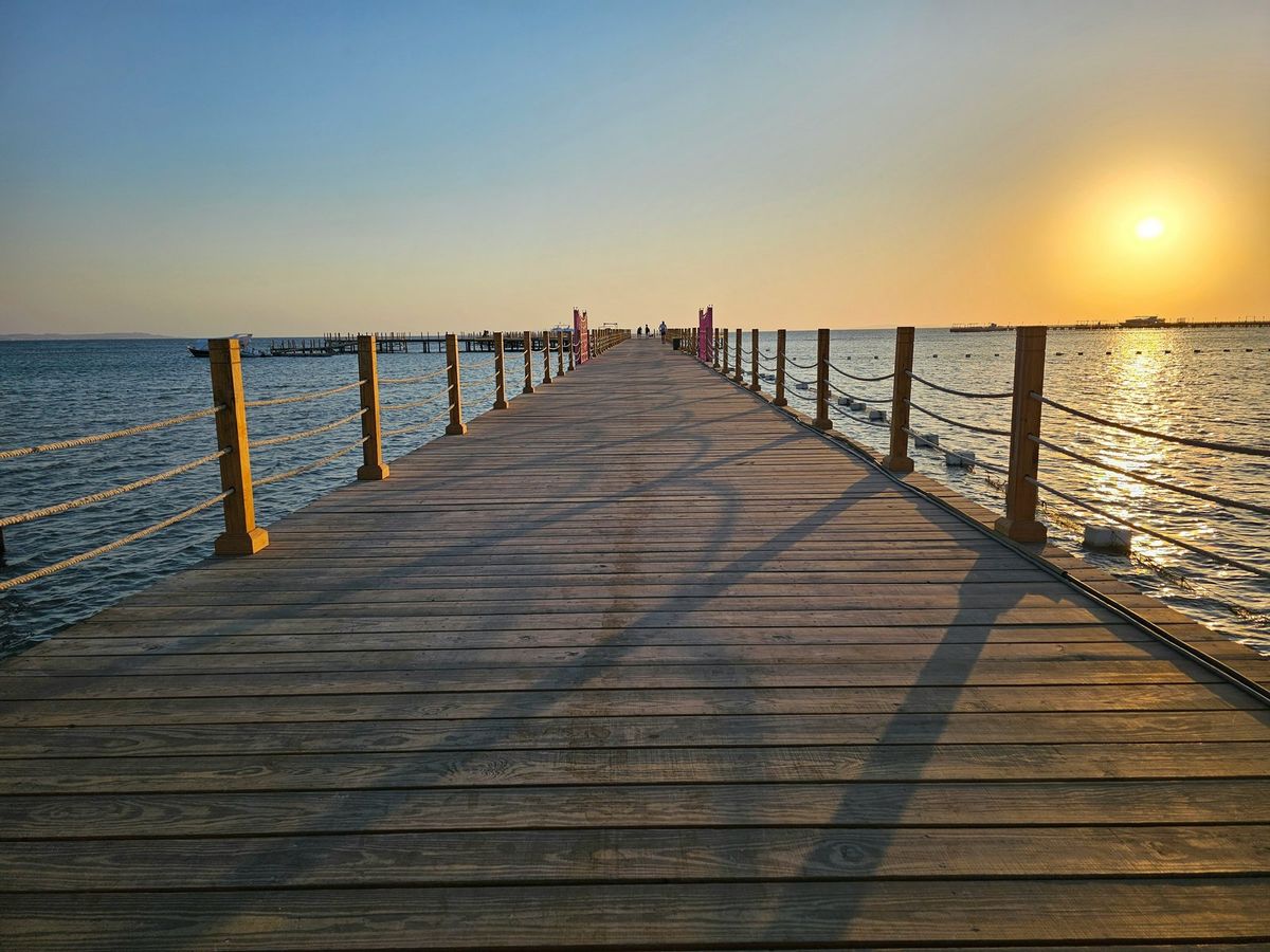 Langer Holzsteg führt bei Sonnenaufgang auf das ruhige Meer hinaus