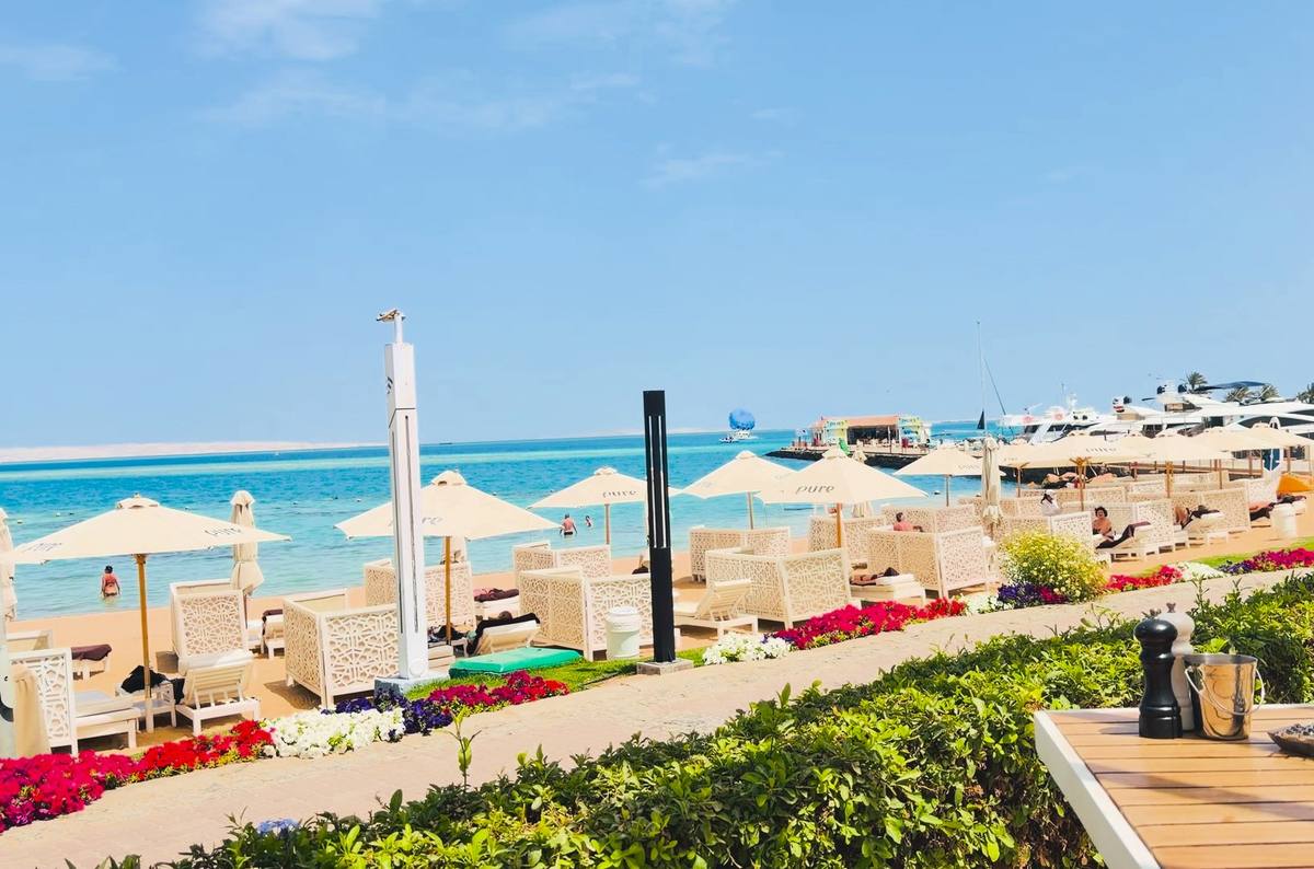 Weiße Sonnenschirme mit Pure-Schriftzug und Strandlounges am Strand des Steigenberger Pure Lifestyle