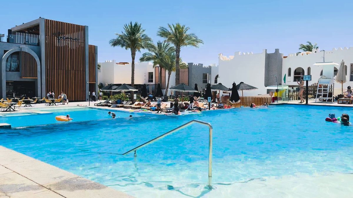 Pool mit Badegästen vor modernen weißen Gebäuden mit Palmen im SUNRISE Tucana in Makadi Bay