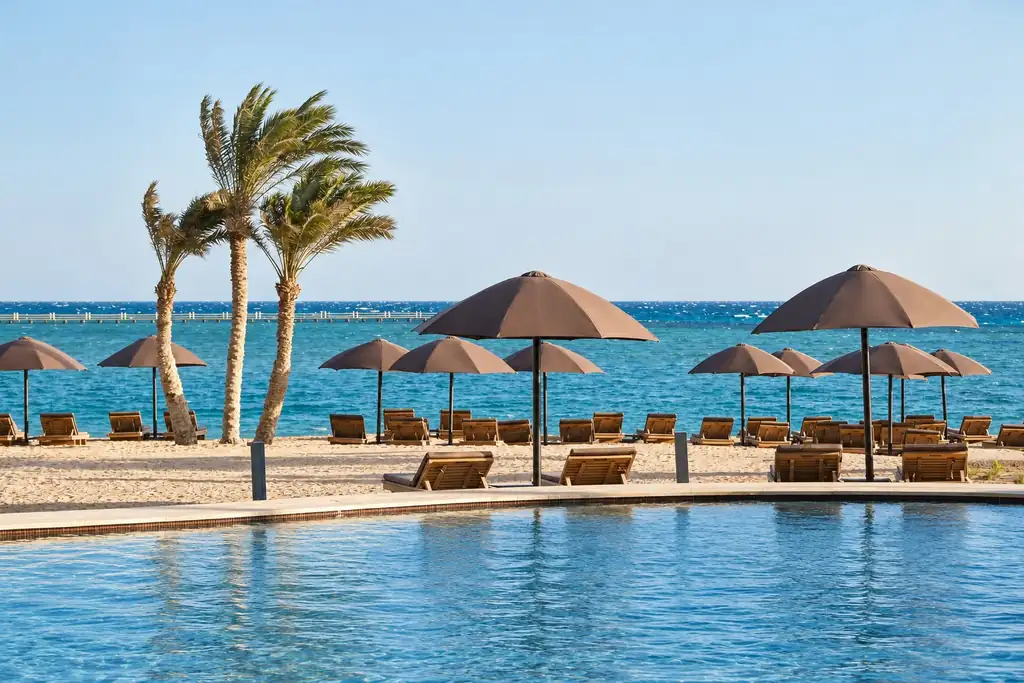 KI-Illustration: Pool und Strand mit braunen Sonnenschirmen im The Chedi El Gouna
