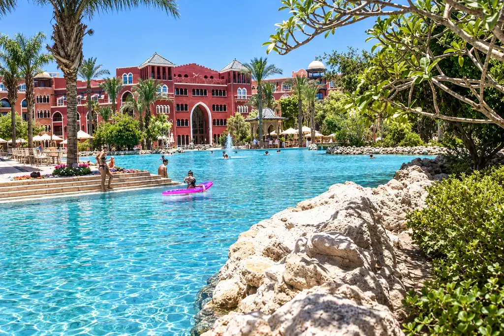 KI-Illustration: Pool vor roter Hotelfassade im The Grand Resort Hurghada