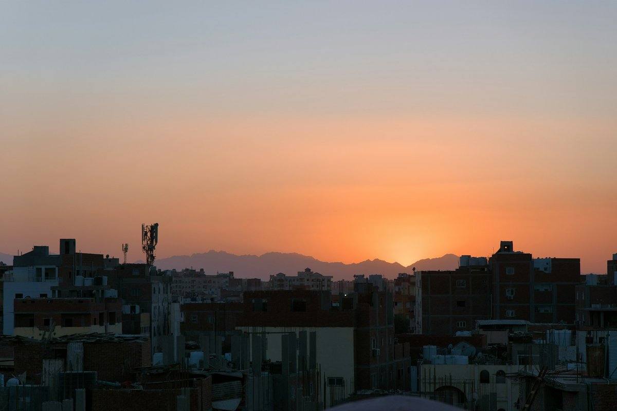 Dächer von Wohnhäusern in Hurghada bei Sonnenuntergang, dahinter die Silhouette der Berge im orangen Abendhimmel